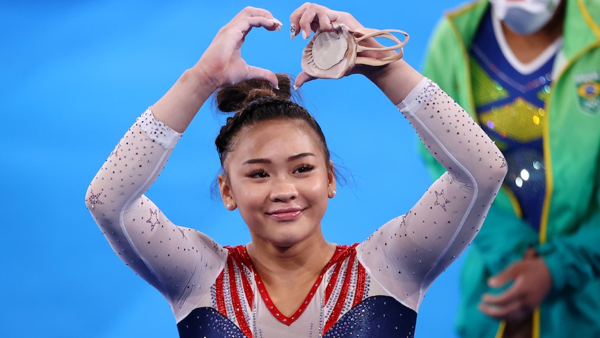 A female gymnast holds up her hands making a love heart shape.