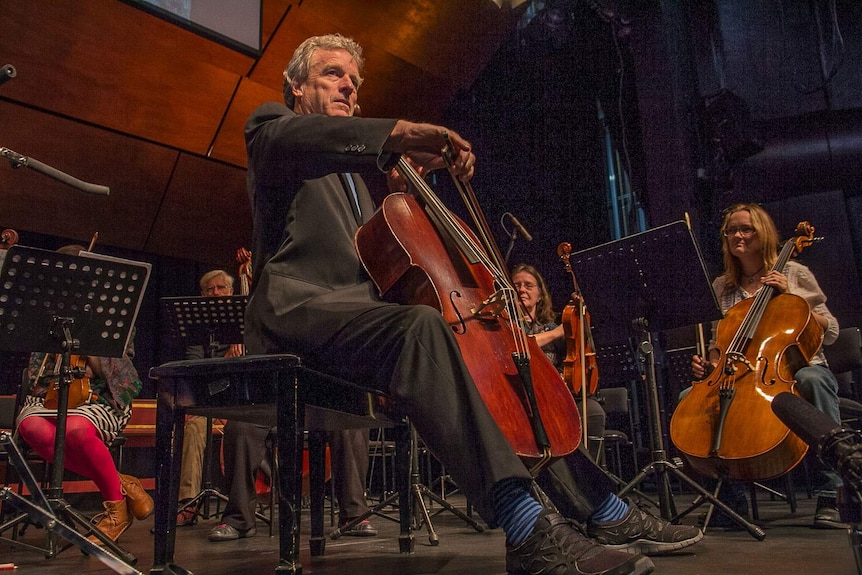 A cellist playing in a concert hall surrounded by other string players