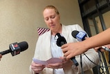 A woman reads a piece of paper into microphones.