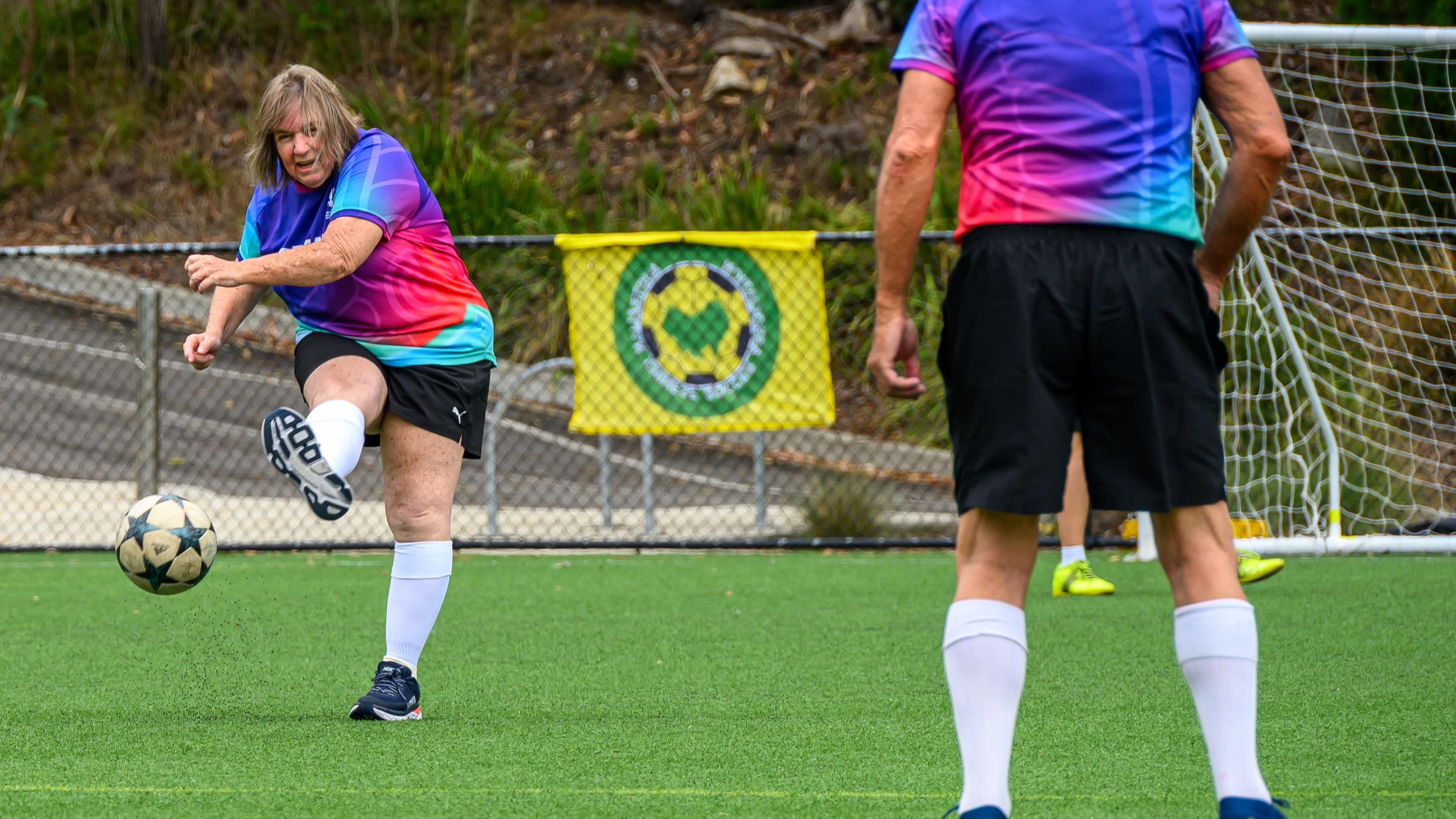 Uma mulher mais velha chuta a bola durante um jogo de futebol