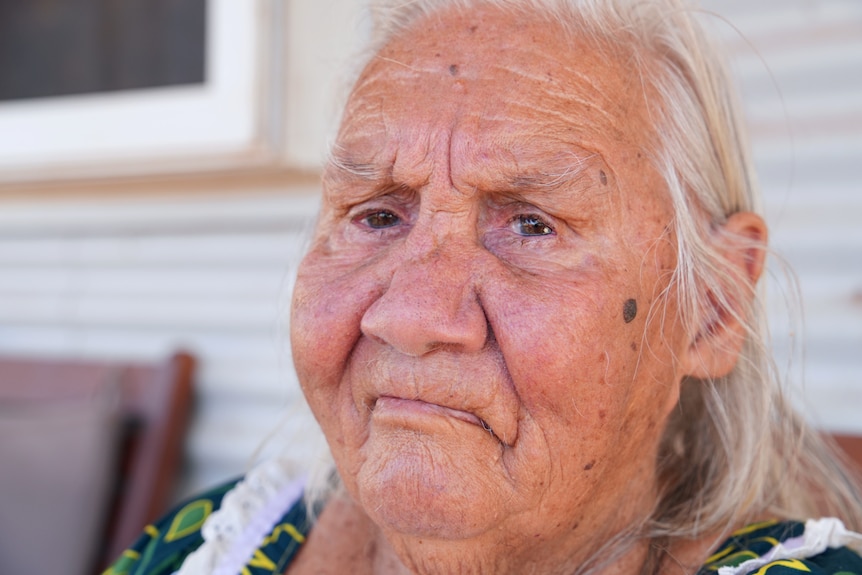 A close up shot of an older woman with white hair and a frown.