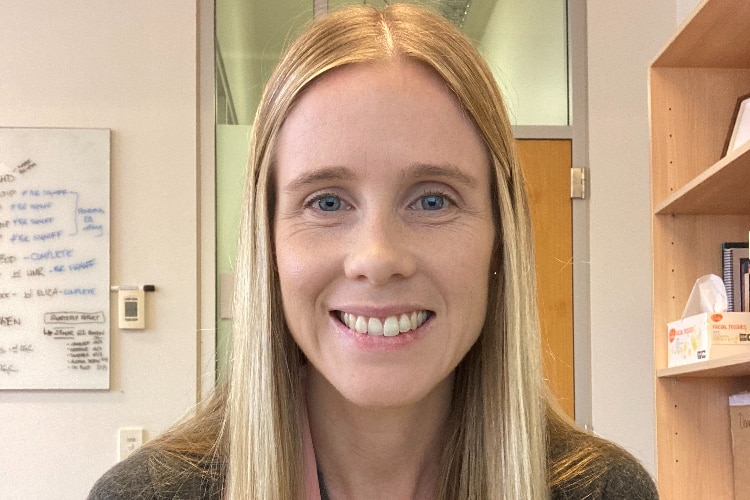 A woman with long blonde hair smiles while sitting in her office.