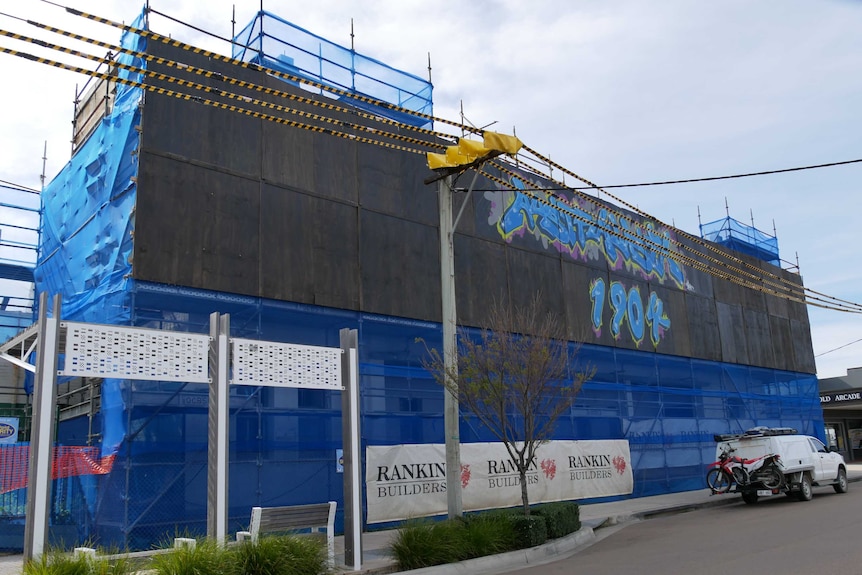 A construction site is covered in a blue mesh and graffiti sign reading 'Australasia 1904'.