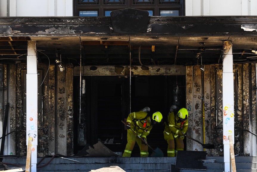 Firefighters clean the damage from a burnt-out doorway.