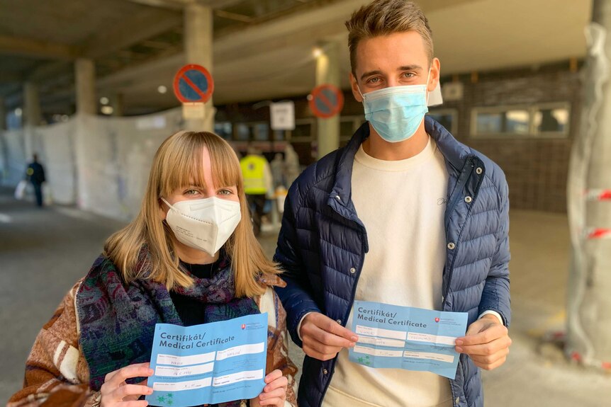 A young woman and a young man in face masks holding medical certificates