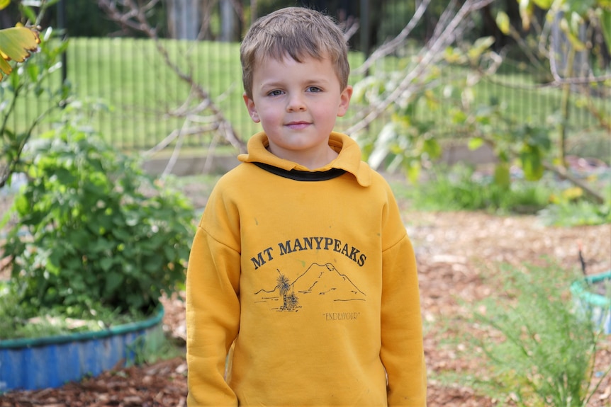 Boy stands in garden in yellow school uniform.