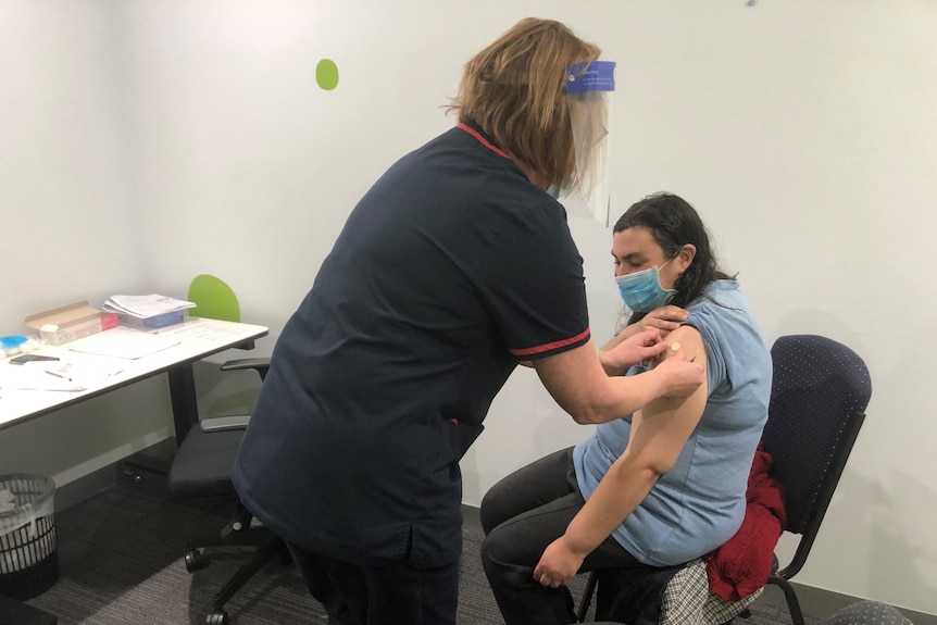 A woman sits on an officer chair receiving a vaccination