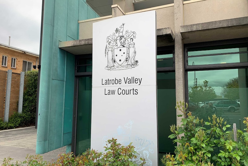 A sign in front of grey building with large class windows reads 'Latrobe Valley Law Courts'.