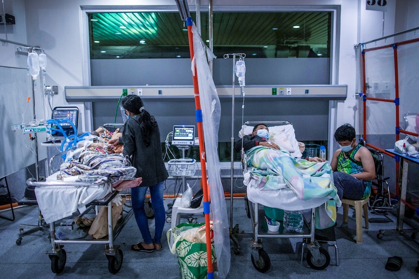 Dwóch pacjentów leżących w łóżkach szpitalnych oddzielonych przeźroczystą tkaniną wiszącą w formie zasłony