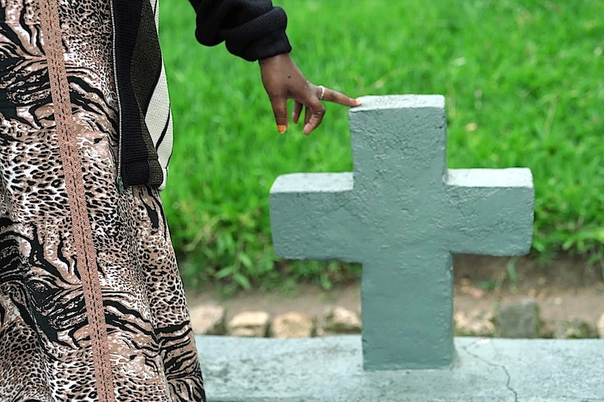 A woman's hand touching a gravestone cross. 