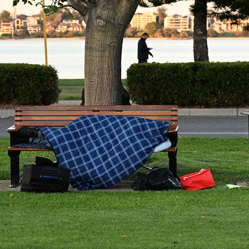 A homeless person sleeping on a park bench in a sleeping bag.