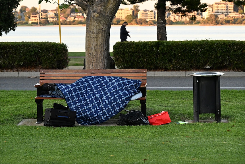 A homeless person sleeping on a park bench in a sleeping bag.