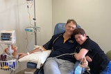 A woman hugs her husband who is hooked up to an IV in hospital.  