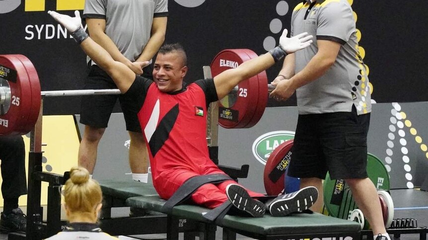 man celebrating beneath a set of bench weights with helpers around him