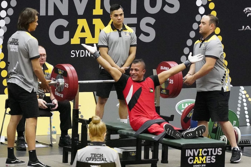 man celebrating beneath a set of bench weights with helpers around him