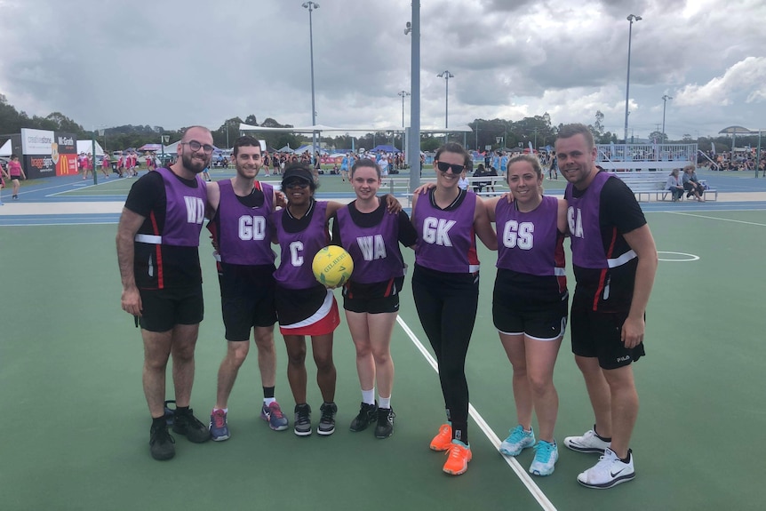 Players wear black clothing and purple netball bibs as they stand with their arms around each other