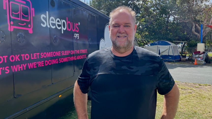 Mark Ellis stands in front of the large pink bus converted into sleeping pods.