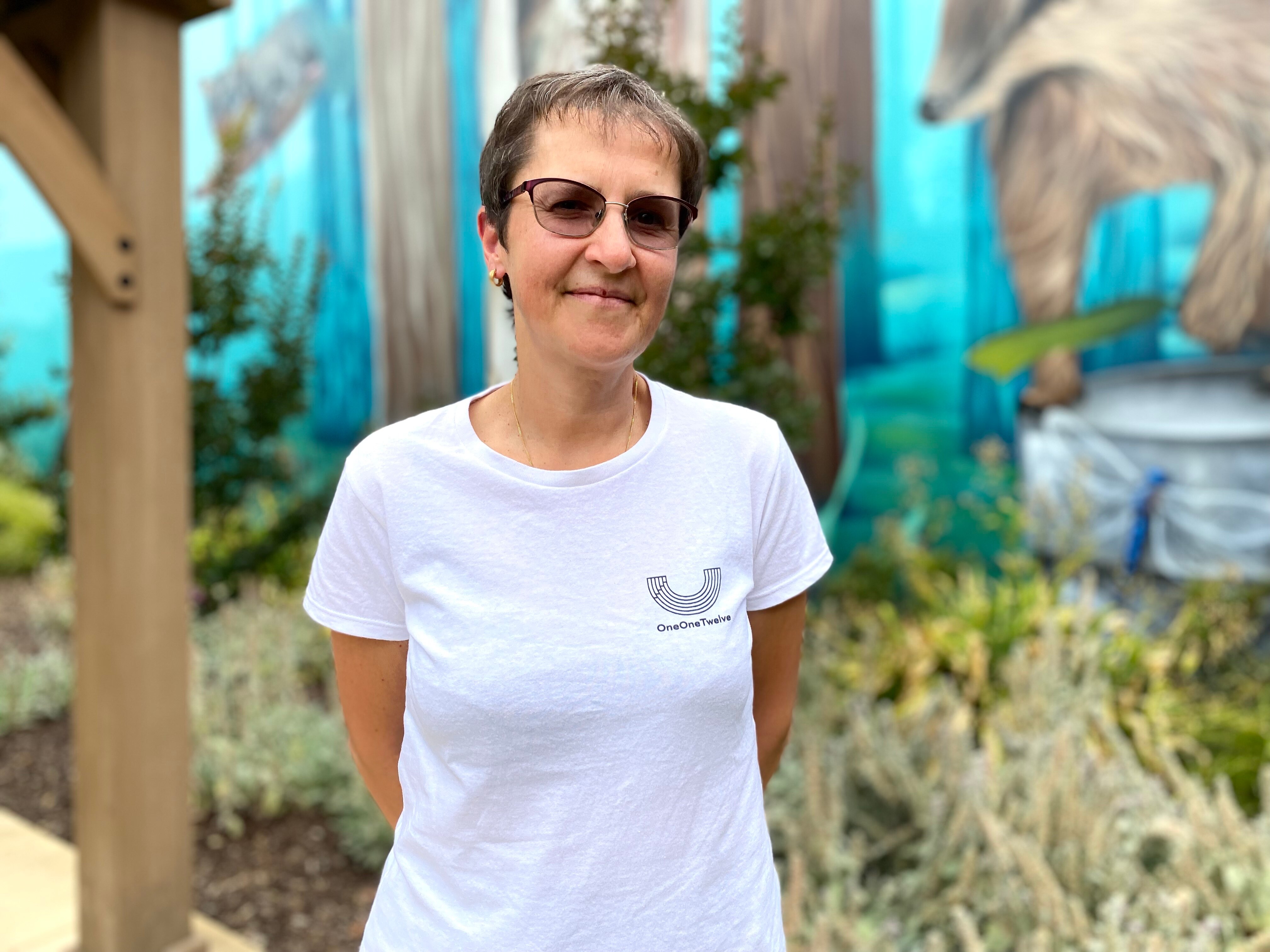 Mina Borromeo stands in front of a mural outside, looking calmly at the camera.