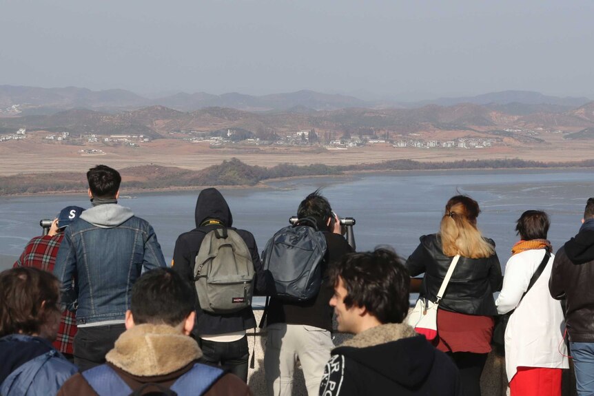 A group of people look at land across a stretch of water.