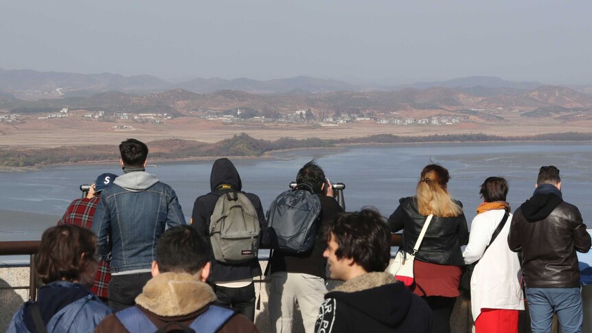 A group of people look at land across a stretch of water.