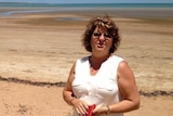 A woman standing on a beach holding her wallet.