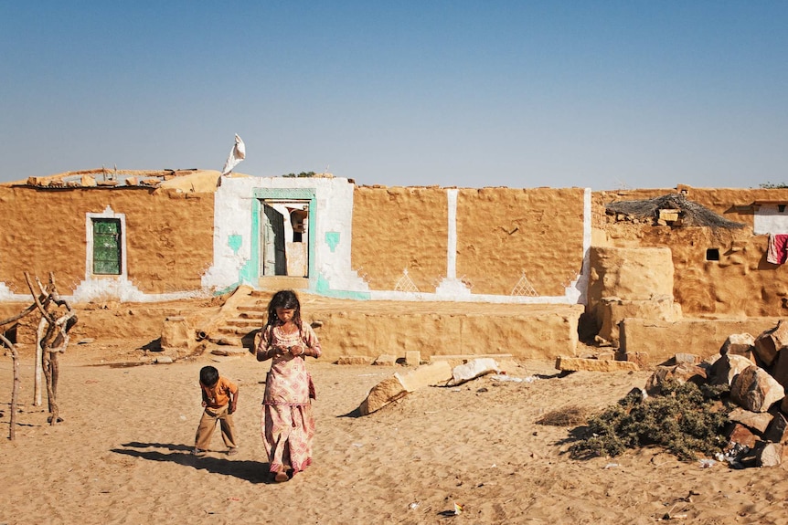 A mud brick house with two children out the front of it