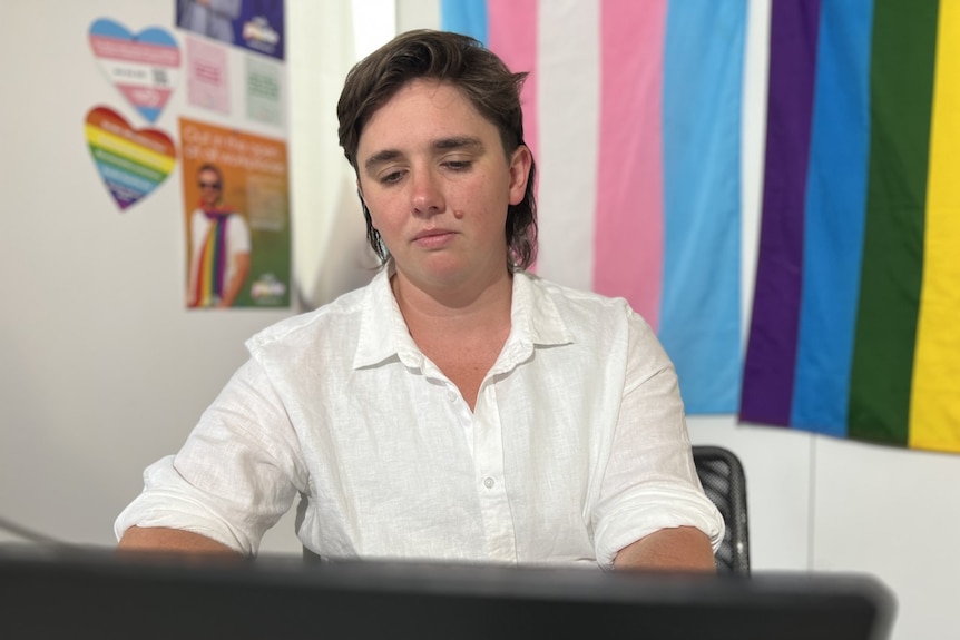 Young person in a white shirt with pride colours in the background