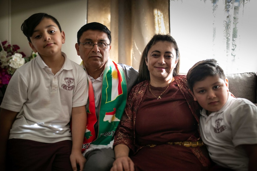 A husband and wife sit for a photo in their home with their two sons.