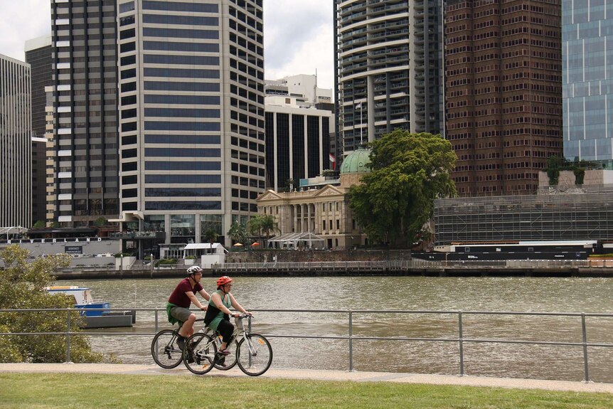 Two cyclists ride by the Brisbane River