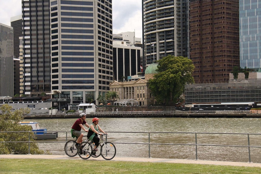 Two cyclists ride by the Brisbane River