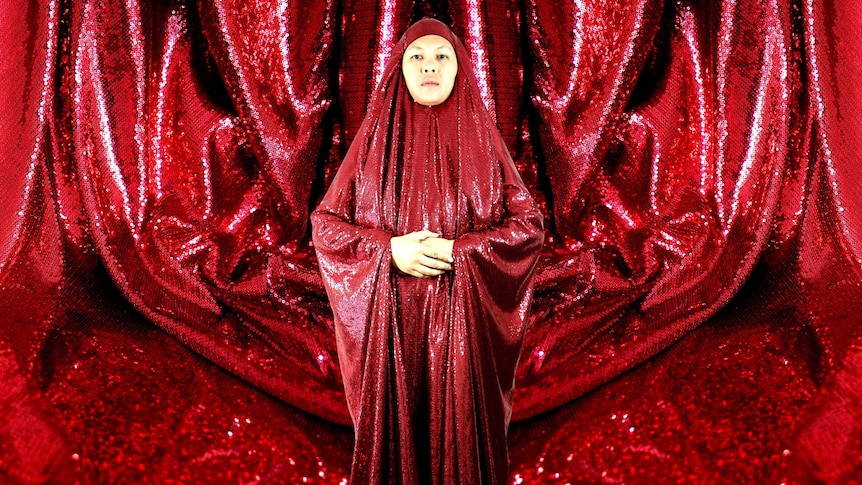 An asian woman in a large red sequinned body covering, the material is also used in the background