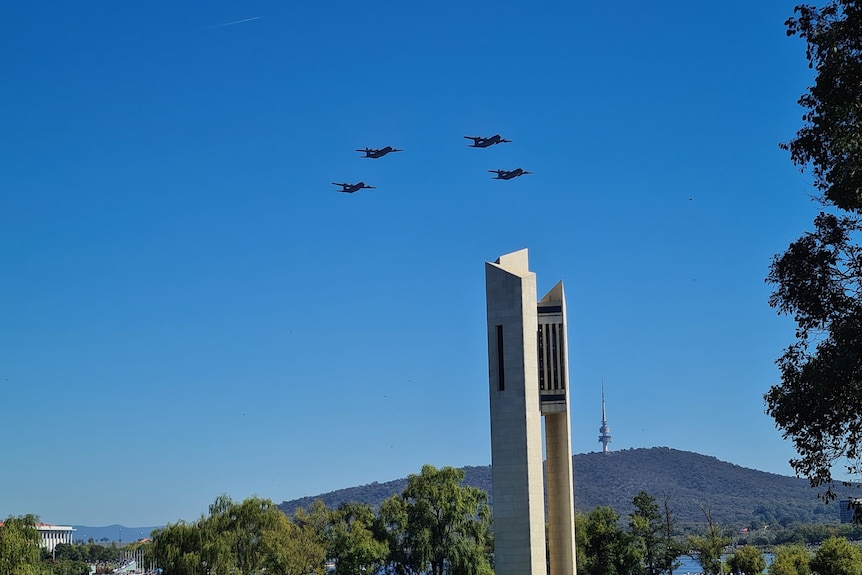 Four planes fly in formation near the Carillon in Canberra, against a bright blue sky.