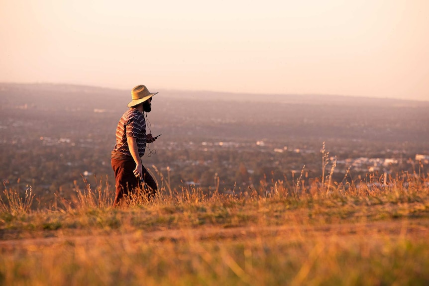 A man walks along a hilltop holding a phone.