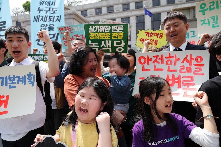 Environmental activist chant and wave signs with Korean writing outside a courthouse. 