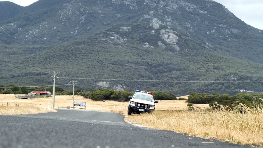 A police care is seen on the side of a road. A big mountain reaches up behind it in the distance.