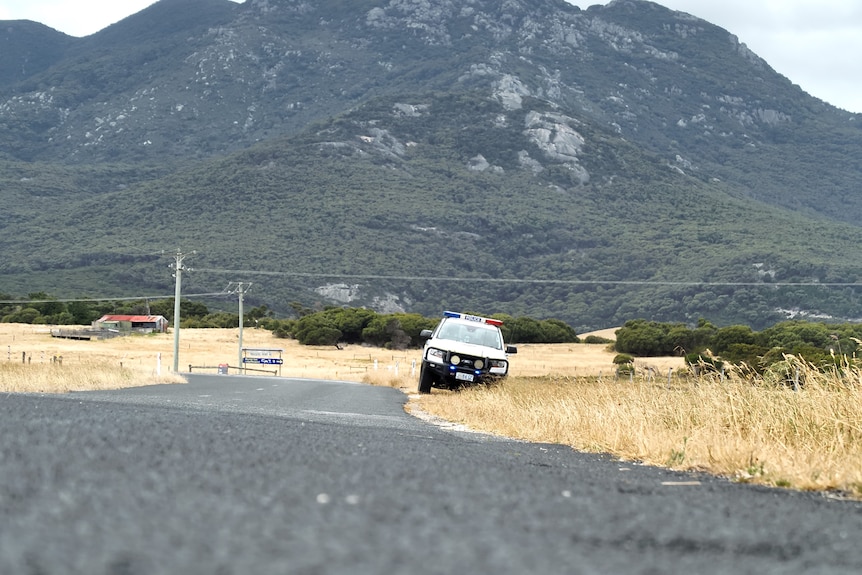 A police care is seen on the side of a road. A big mountain reaches up behind it in the distance.