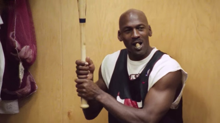 Michael Jordan holds a baseball bat and smokes a cigar in the Chicago Bulls' locker room.