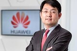 Huawei executive Walter Ji standing in front of a TV screen featuring the company's logo.