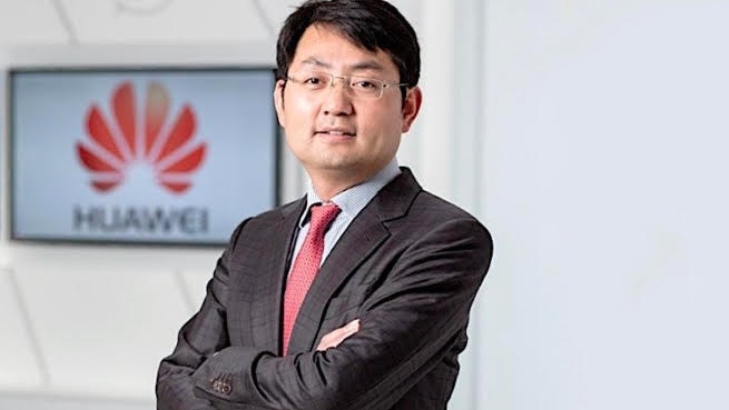 Huawei executive Walter Ji standing in front of a TV screen featuring the company's logo.