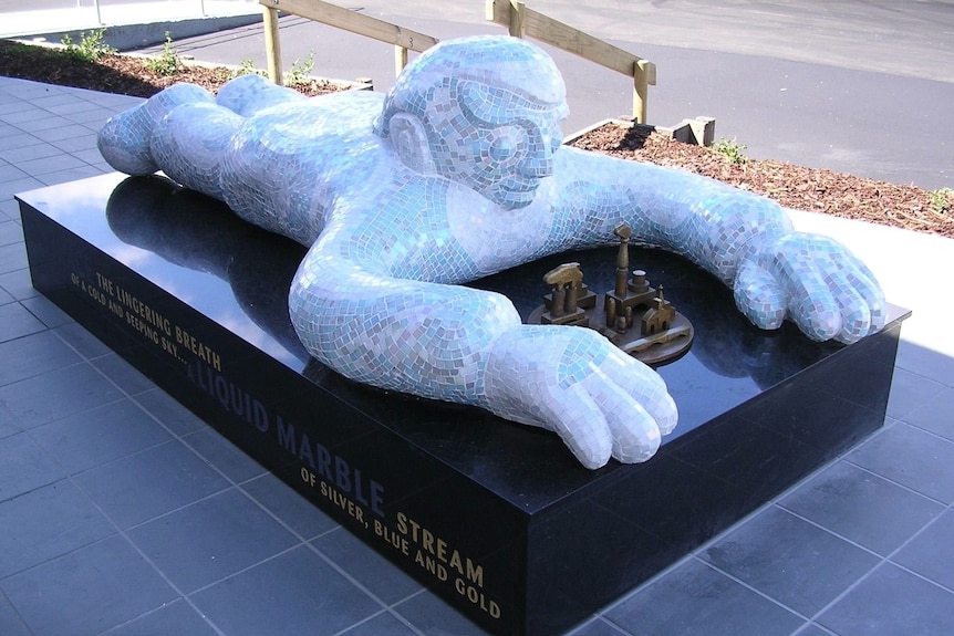 A blue statue of a male figure lying on his stomach