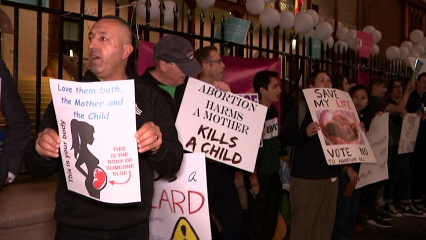 People hold up pro-life signs at the gates of Parliament house.