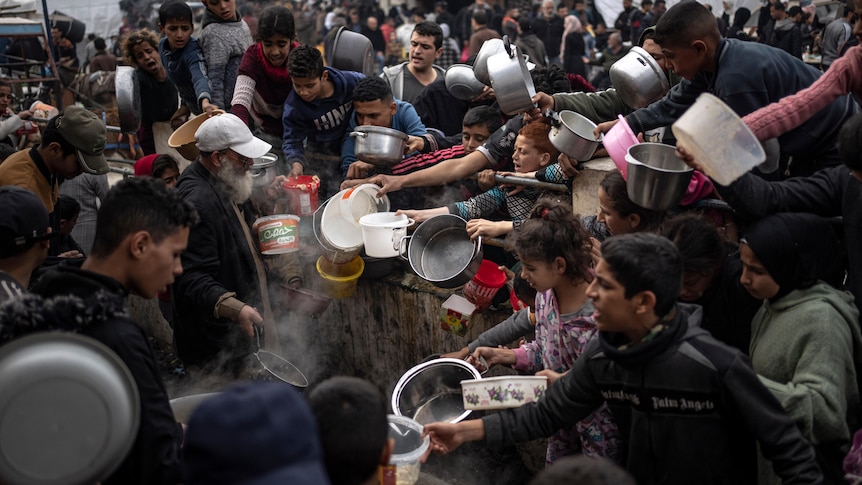 People crowd together holding empty containers to fill with food.