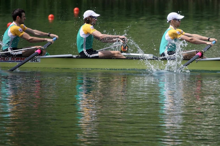 Three men in a green, yellow and white uniforms stroke together on a rowing boat.