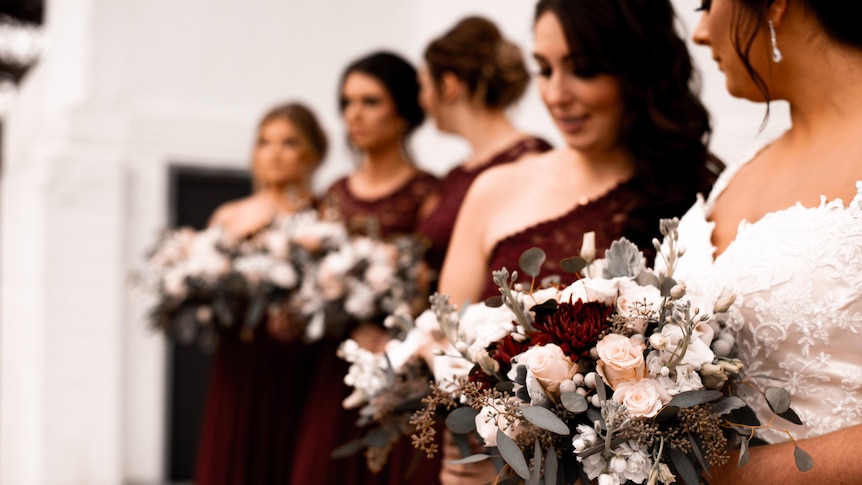 Four bridesmaids in deep red dresses hold flowers next to a bride with dark hair