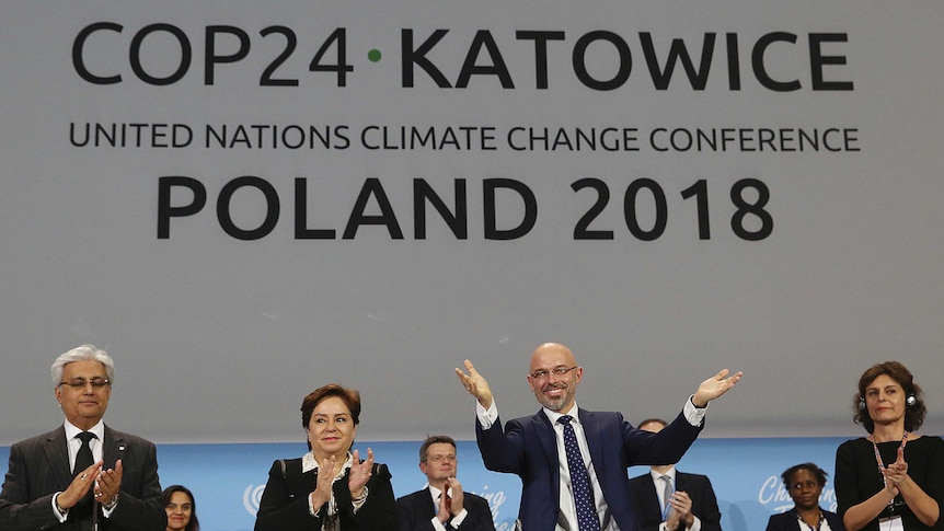 Poland's Michal Kurtyka and UN officials celebrate onstage during UN climate talks with its logo in the background.