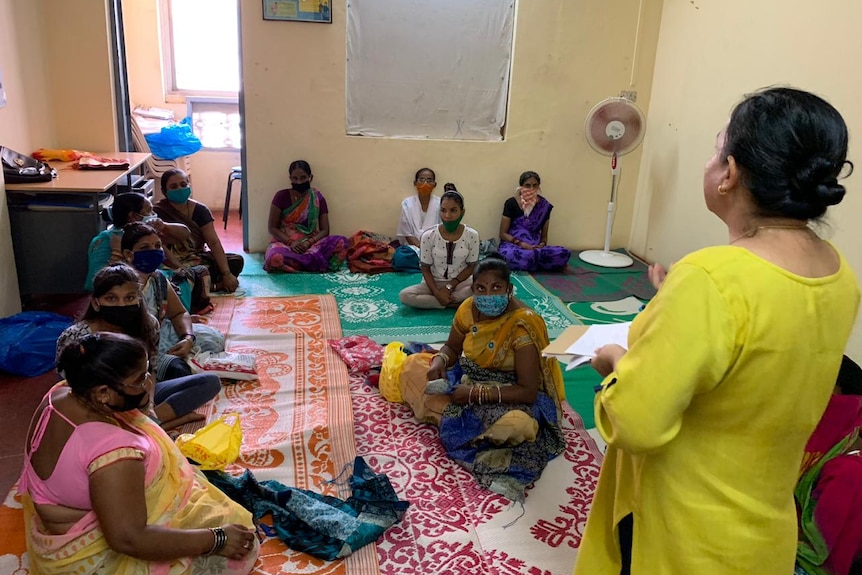 A group of women wearing mask sitting on the floor and listen to an instruction.