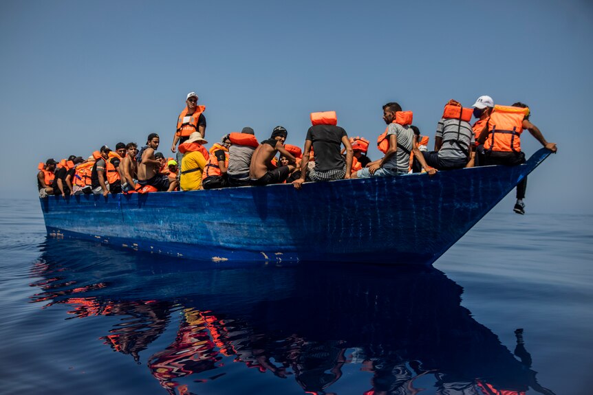 Dozens of men on a small, blue fishing boat.