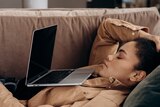 Woman looking exhausted in front of laptop on couch