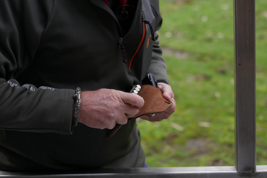 a close shot of a mans hands pulling rifle bullets from a leather pouch
