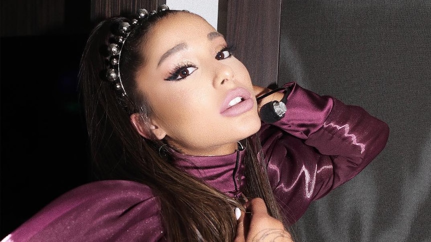 Ariana Grande wears a purple dress and does a pose.